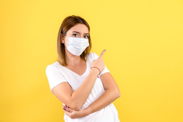 Front view of young woman in mask on yellow wall