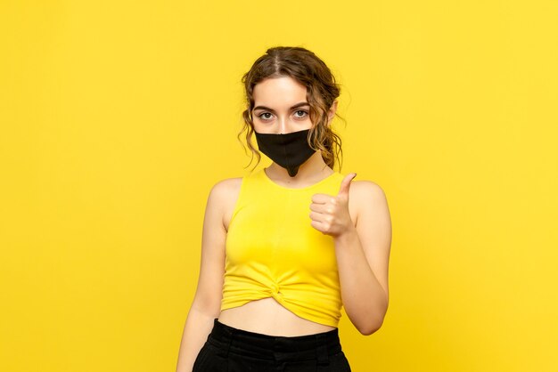 Front view of young woman in mask on a yellow wall