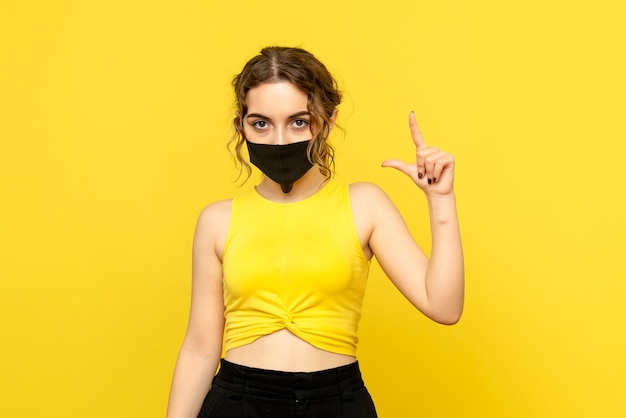 Front view of young woman in mask on a yellow wall