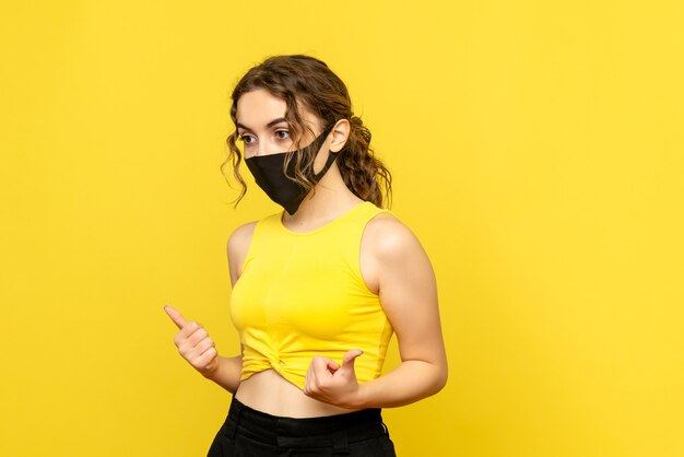 Front view of young woman in mask on a yellow wall