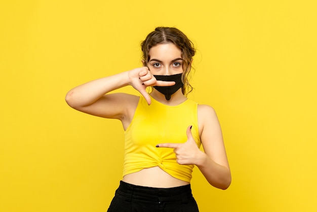 Vista frontale della giovane donna in maschera sulla parete gialla