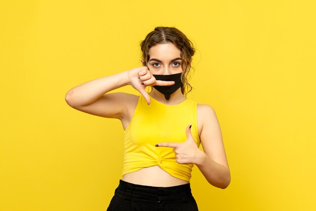 Front view of young woman in mask on yellow wall