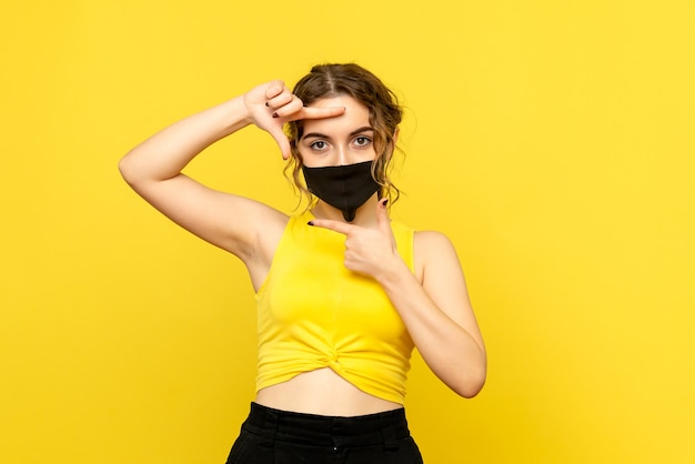 黄色の壁にマスクで若い女性の正面図