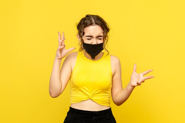 Front view of young woman in mask on yellow wall