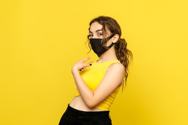 Front view of young woman in mask on yellow wall