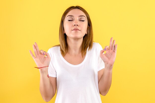 Front view of young woman meditating on yellow wall