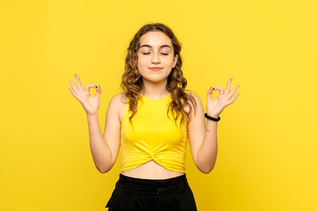 Front view of young woman meditating on yellow wall