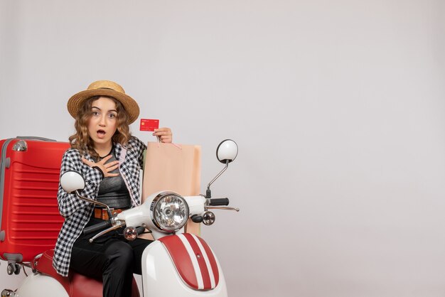 Front view young woman on moped holding card and shopping bag putting hand on her chest