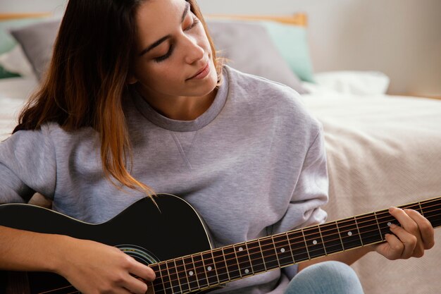 Front view of young woman playing guitar at home