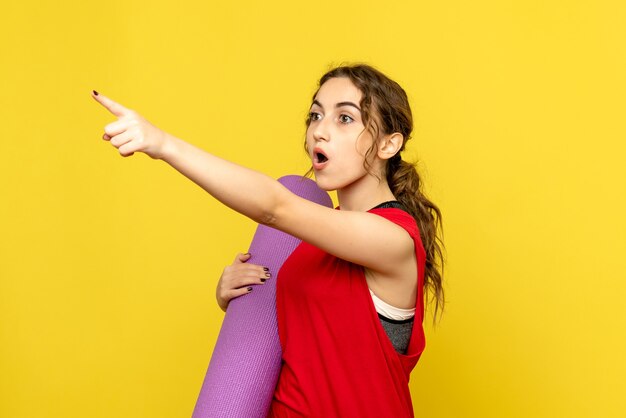 Front view of young woman pointing at distance on yellow wall