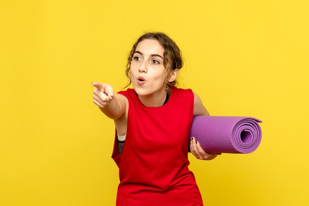 Front view of young woman pointing with purple carpet on yellow wall