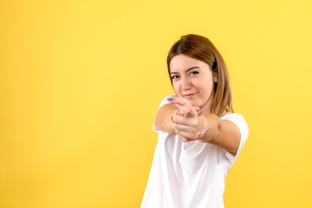 Front view of young woman pointing on yellow wall
