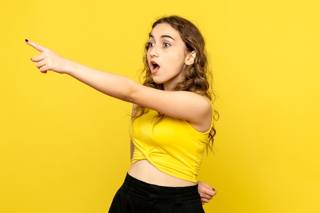 Front view of young woman pointing on yellow wall
