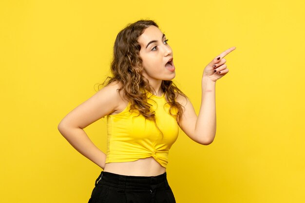 Front view of young woman pointing on yellow wall