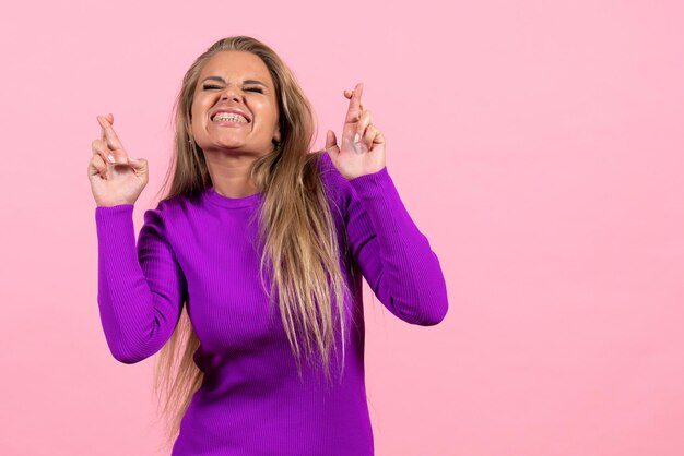 Front view of young woman posing in beautiful purple dress on the pink wall