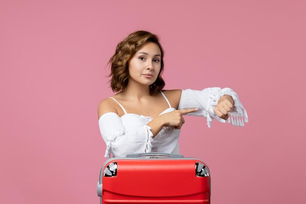 Front view of young woman posing and checking time on pink wall