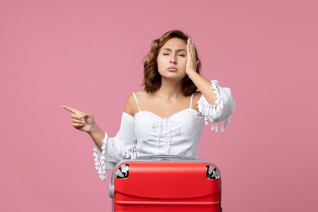 Front view of young woman posing with red vacation bag on a pink wall