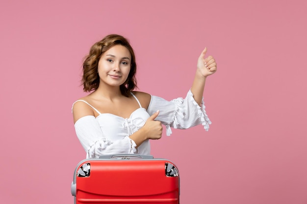Front view of young woman posing with red vacation bag on pink wall