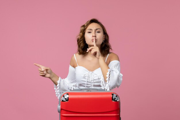 Front view of young woman posing with red vacation bag on pink wall