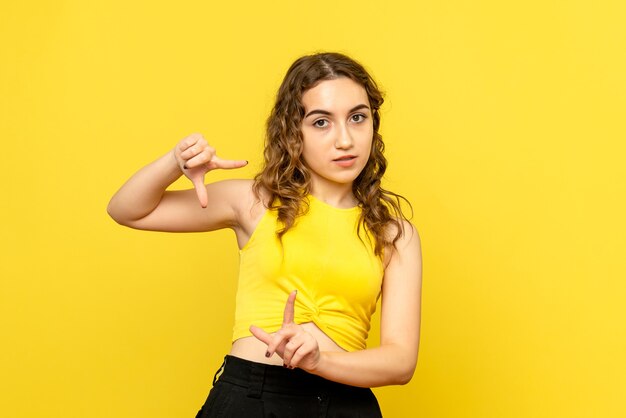 Front view of young woman posing on yellow wall