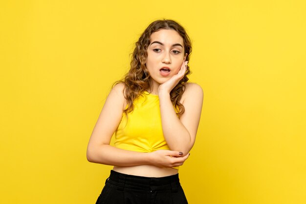 Front view of young woman posing on yellow wall