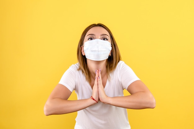 Front view of young woman praying in mask on yellow wall