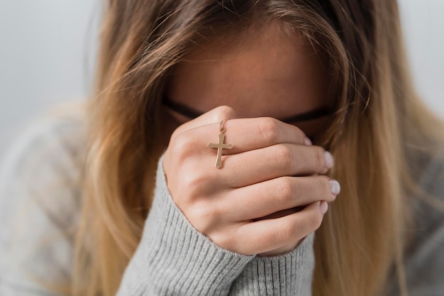 Front view of young woman praying while holding cross necklace