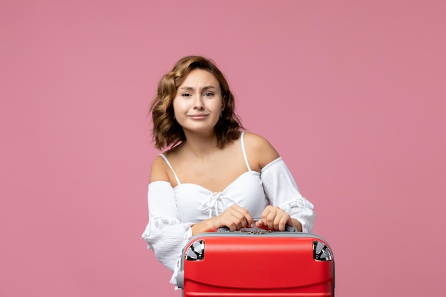 Front view of young woman preparing for summer trip with red bag on pink wall