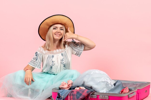 Вид спереди молодая женщина, готовящаяся к поездке и разбирающая свою одежду на розовом фоне, поездка, путешествие, отдых, цветная одежда