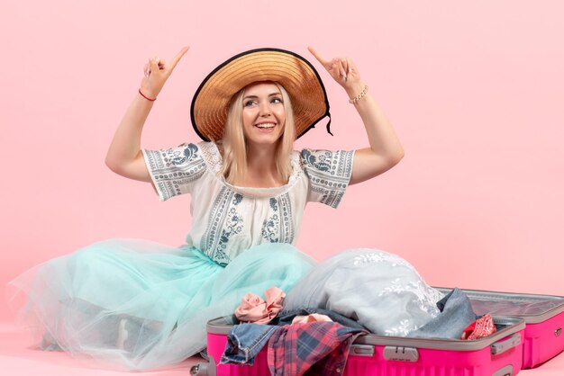 Front view young woman preparing for trip and disassembling her clothes on pink desk trip voyage vacation sea plane rest color