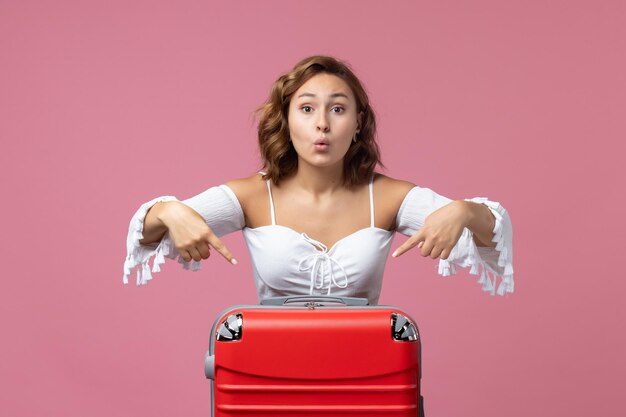 Front view of young woman preparing for trip with red bag on a pink wall