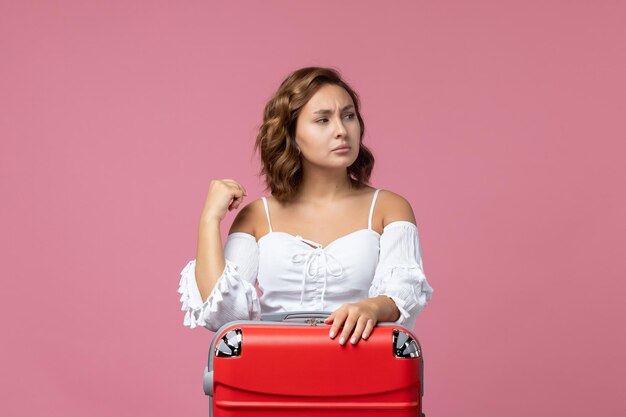 Front view of young woman preparing for trip with red bag on a pink wall