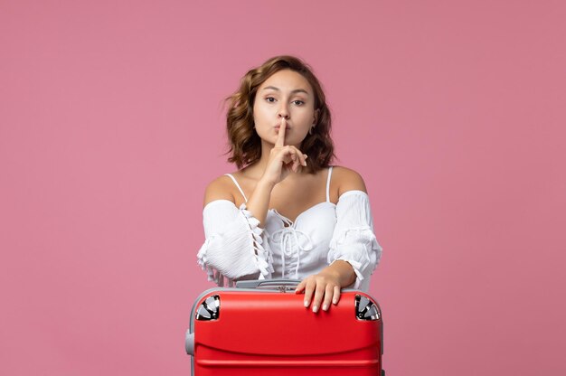 Front view of young woman preparing for trip with red bag on pink wall