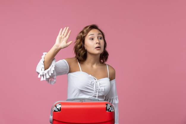 Front view of young woman preparing for trip with red bag on pink wall