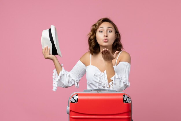 Front view of young woman preparing for vacation and holding hat on pink wall