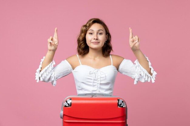 Front view of young woman preparing for vacation with bag and smiling on pink wall