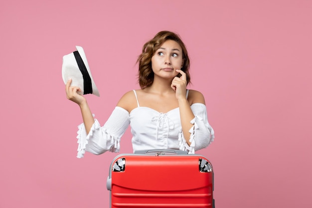 Vista frontale della giovane donna che si prepara per le vacanze con una borsa rossa in posa sul muro rosa