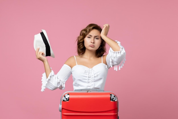 Front view of young woman preparing for vacation with red bag and posing on the pink wall