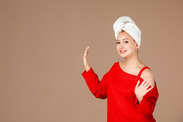 front view of young woman in red shirt with towel on her head on brown wall