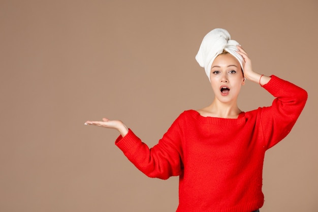 front view of young woman in red shirt with towel on her head on brown wall