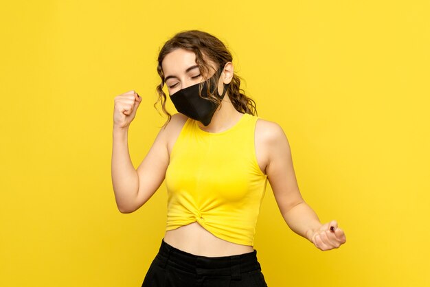 Front view of young woman rejoicing in mask on yellow wall