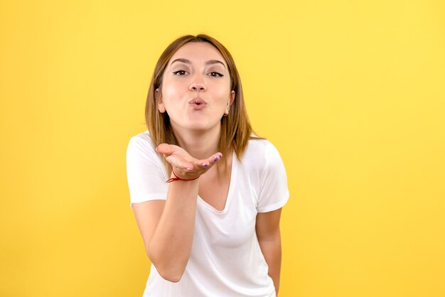 Front view of young woman sending air kisses on yellow wall