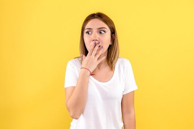 Front view of young woman shocked on yellow wall