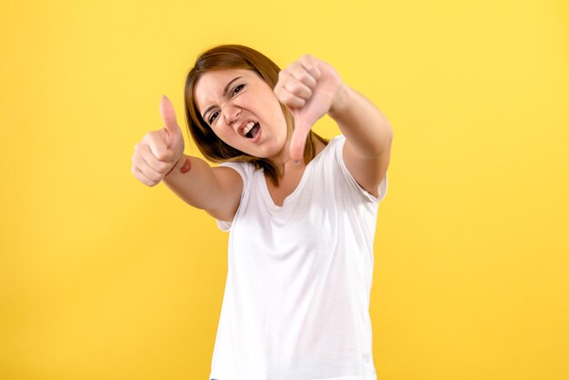 Front view of young woman showing signs on yellow wall