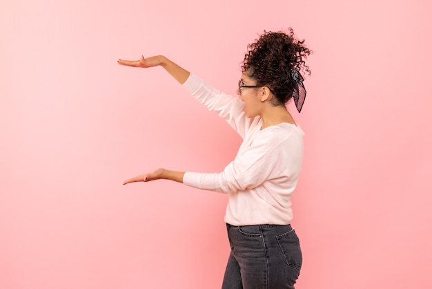 Foto gratuita vista frontale della giovane donna che mostra le dimensioni sulla parete rosa chiaro