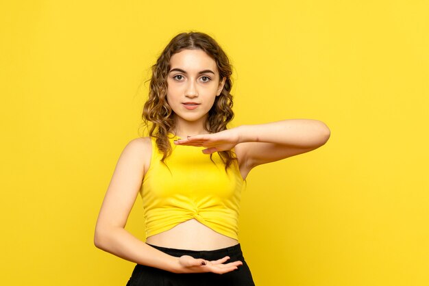 Front view of young woman showing size on yellow wall