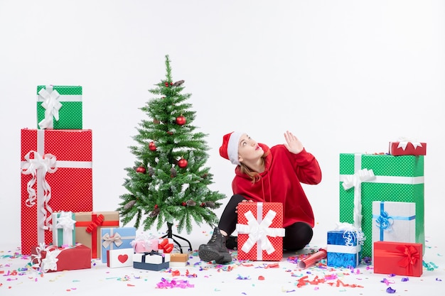 Front view of young woman sitting around holiday presents on a white wall