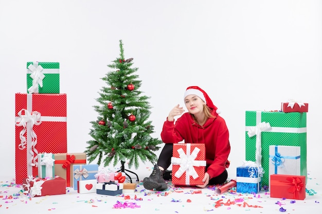 Вид спереди молодой женщины, сидящей вокруг праздничных подарков на белой стене