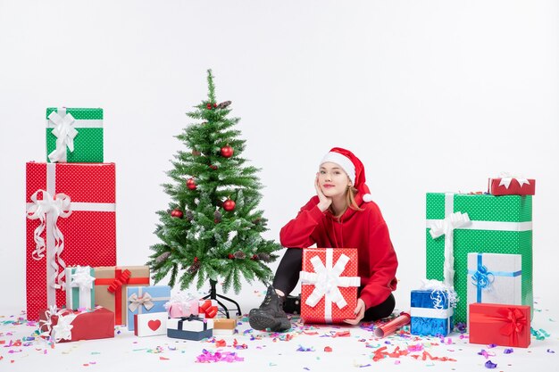 휴일 주위에 앉아있는 젊은 여자의 전면보기 흰 벽에 선물