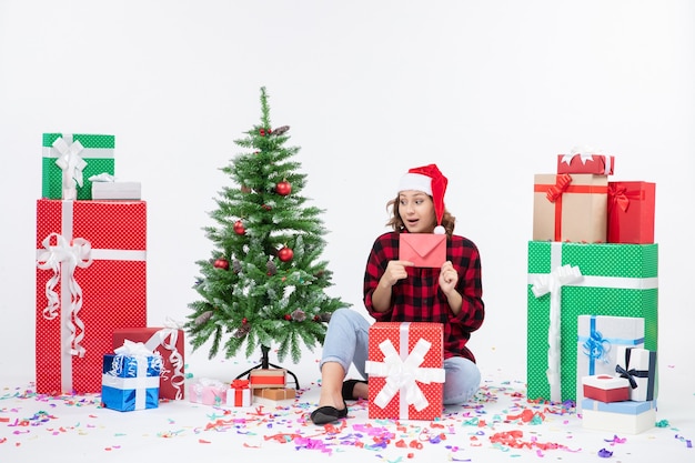 Front view of young woman sitting around presents holding envelop on a white wall